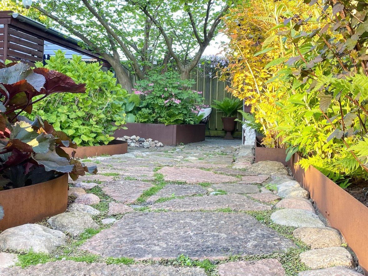 Beeteinfassung aus Cortenstahl entlang eines Naturstein-Gartenwegs – moderne und langlebige Beetkante in Rostoptik