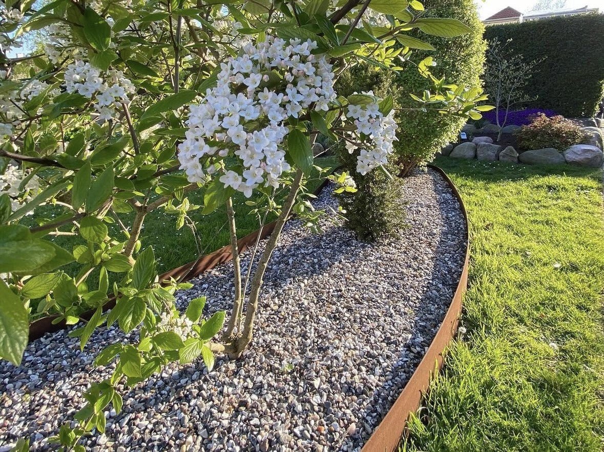 Große geschwungene Rasenkante aus Cortenstahl vor Terrasse und Gewächshaus – moderne Gartenabgrenzung