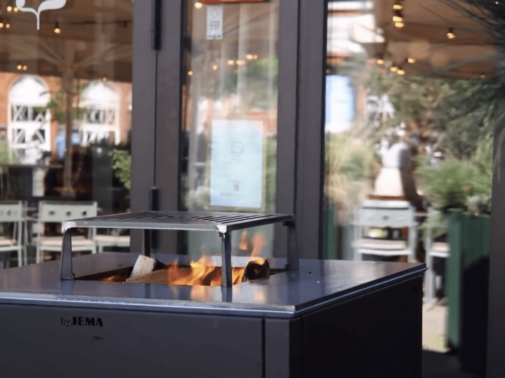 CUBY Feuergrill aus schwarz lackiertem Stahl im Außenbereich eines Restaurants mit Glasfassade