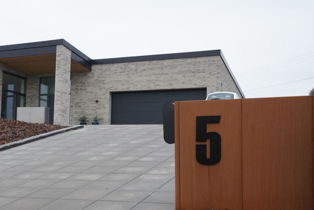 Mülltonnenverkleidung aus Cortenstahl mit großer schwarzer Hausnummer 5 vor moderner Einfahrt