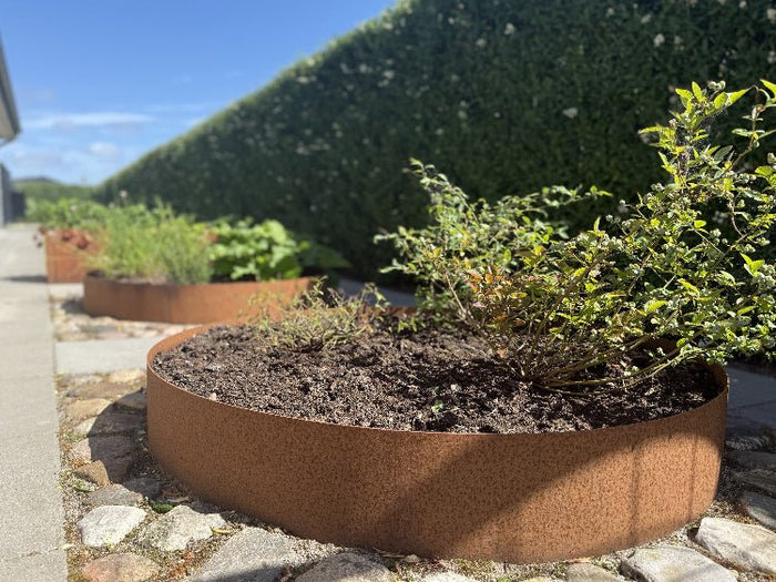 Beeteinfassung aus Cortenstahl mit Pflanzen entlang eines Natursteinwegs im Garten