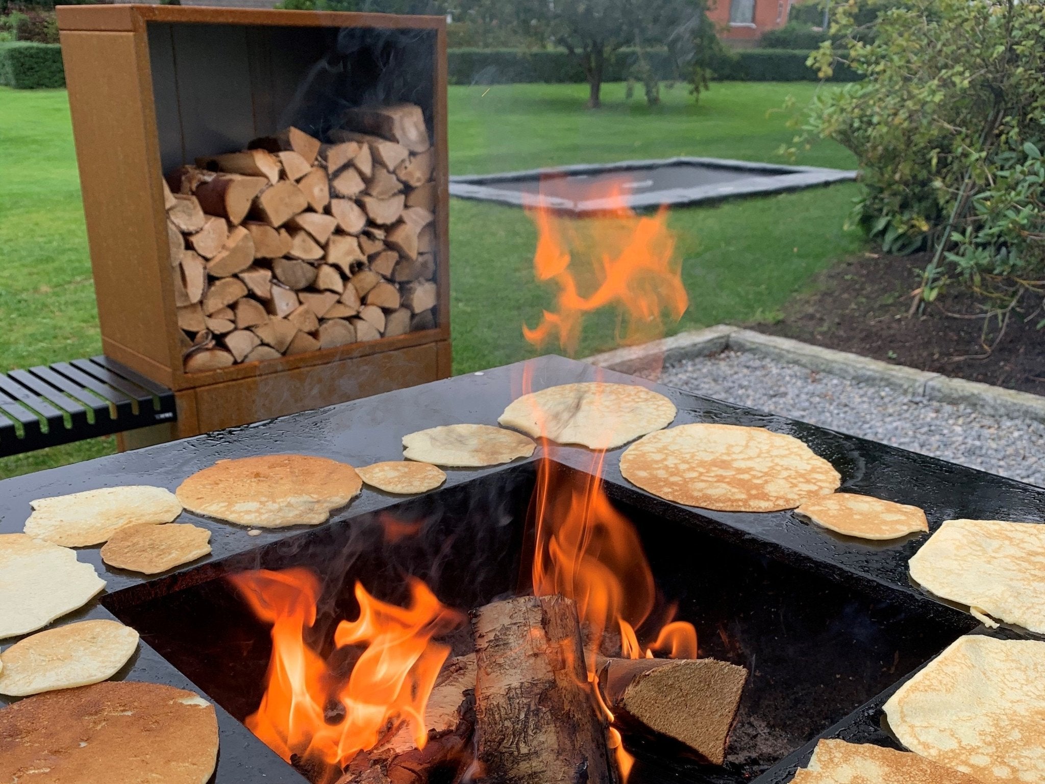 byJEMA Feuerstelle aus Cortenstahl mit Grillplatte – Pfannkuchen werden über offenem Feuer im Garten zubereitet